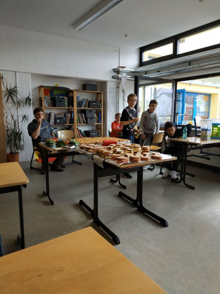 Schüler stehen um mehrere Tische mit Sandwiches und Snacks.