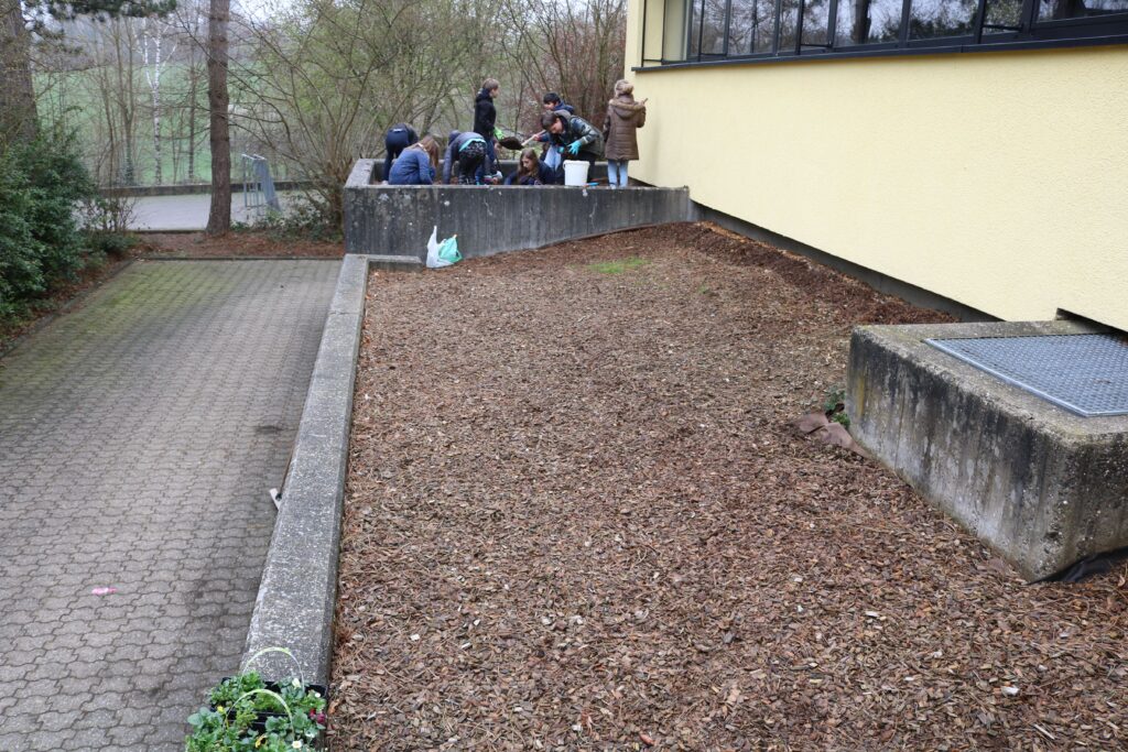 Blick auf einen blühenden Gartenbereich mit mehreren Personen, die arbeiten.