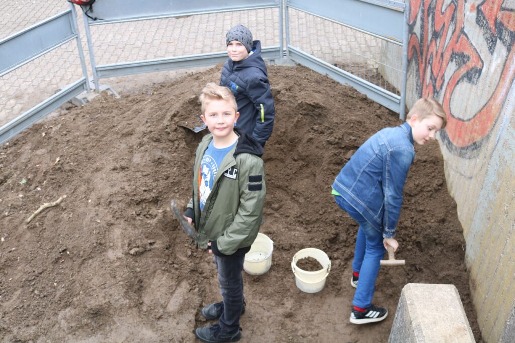 Drei Kinder graben in einem Sandhaufen und arbeiten an einem Projekt.