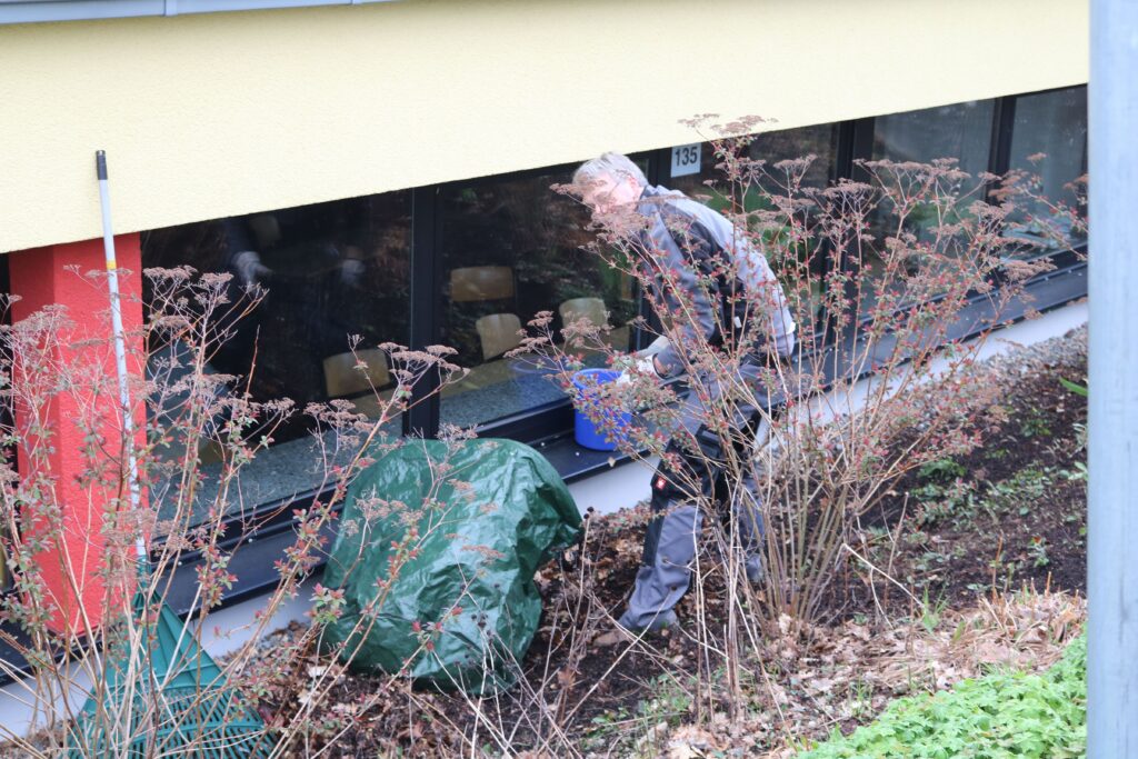 Eine Person arbeitet im Gartenbereich neben einem Gebäude.