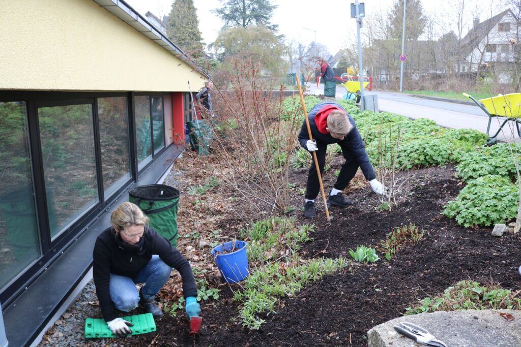 Schüler pflanzen Blumen in einem Garten neben einem Schulgebäude.