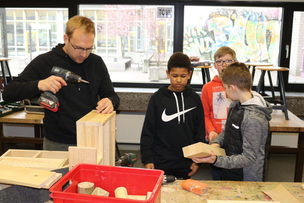 Schüler arbeiten mit einem Lehrer im Werkraum an einem Holzprojekt.