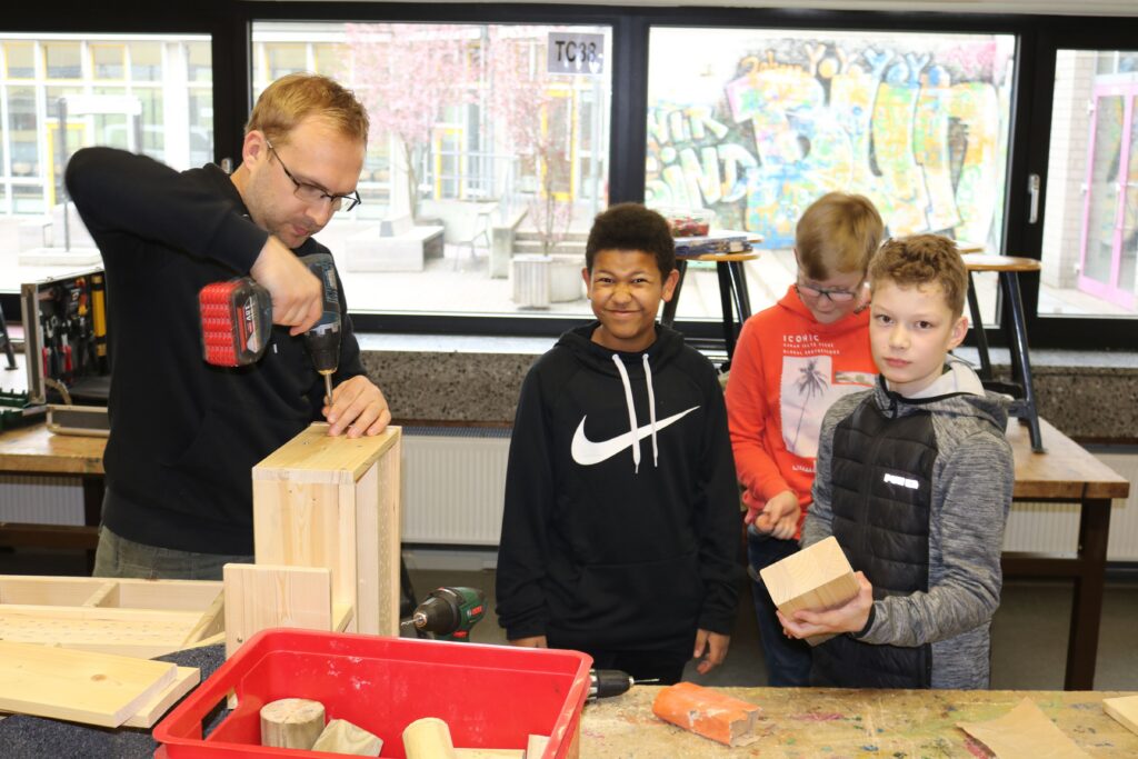 Ein Lehrer zeigt Schülern das Arbeiten mit Holz und Werkzeug.