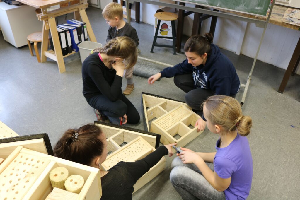 Kinder und Erwachsene arbeiten gemeinsam an Holzspielzeugen in einem Klassenraum.