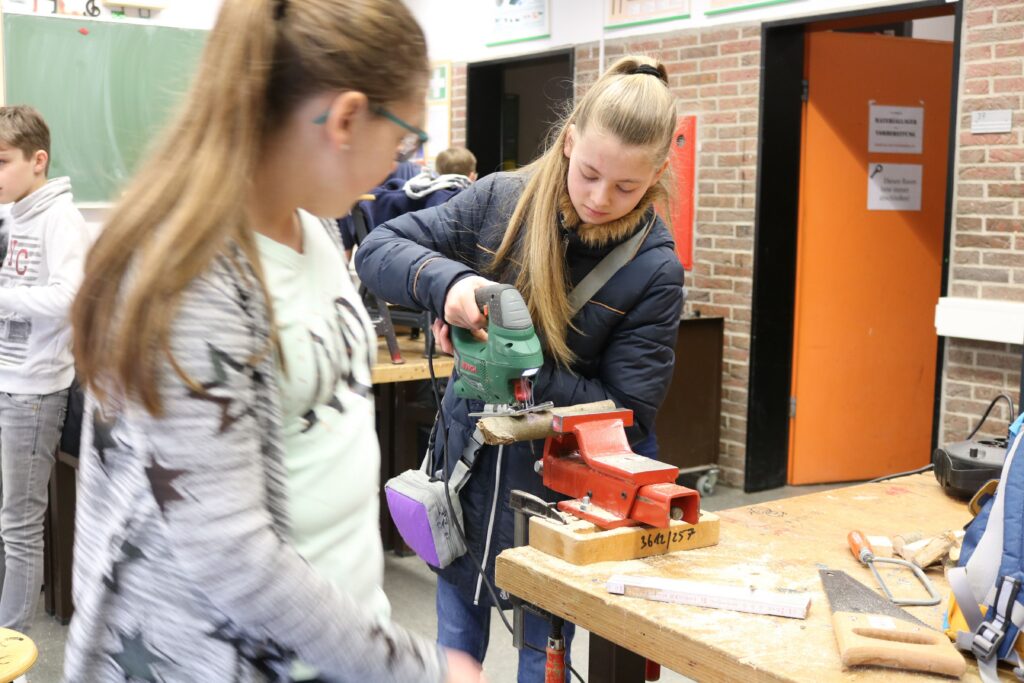 Schülerinnen arbeiten in einer Werkstatt mit Werkzeug an einem Werkstück.