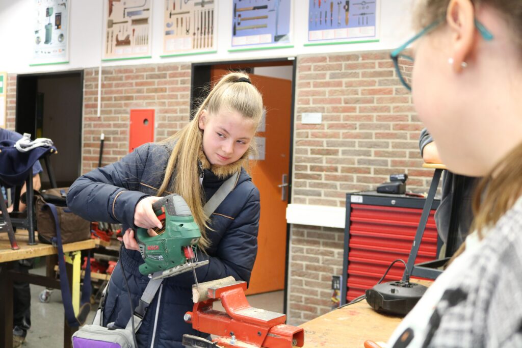 Schülerin bearbeitet Holz mit einer elektrischen Säge in der Werkstatt.