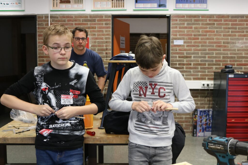 Zwei Schüler arbeiten konzentriert an einem Tisch, im Hintergrund eine Lehrperson.