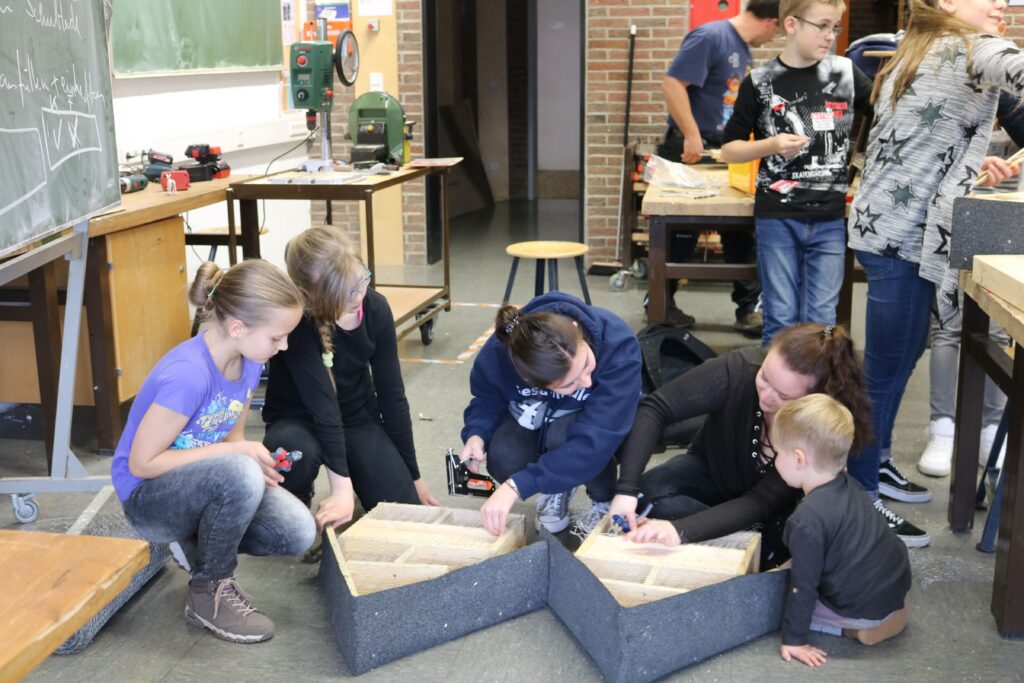 Gruppe von Kindern und Erwachsenen arbeitet gemeinsam an einem Projekt in einem Klassenraum.