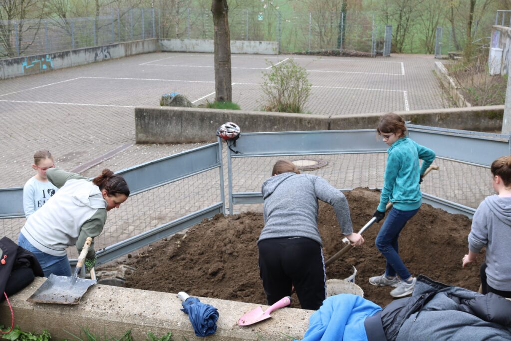Schülerinnen und Schüler graben in einem Sandkasten auf dem Schulgelände.