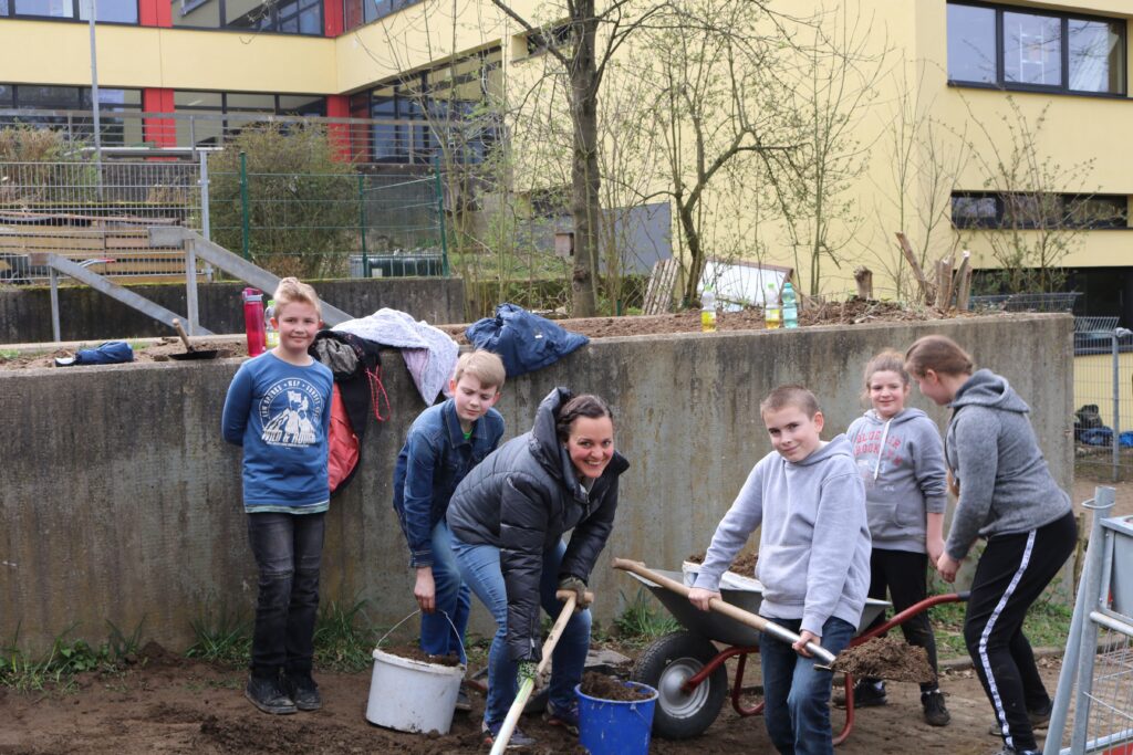 Schülerinnen und Schüler arbeiten im Schulgarten mit Schaufeln und Eimern.