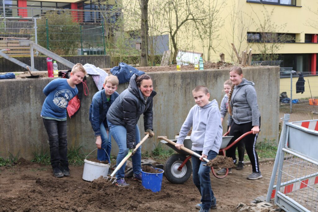 Schüler und Schülerinnen arbeiten gemeinsam im Schulgarten und graben Erde um.