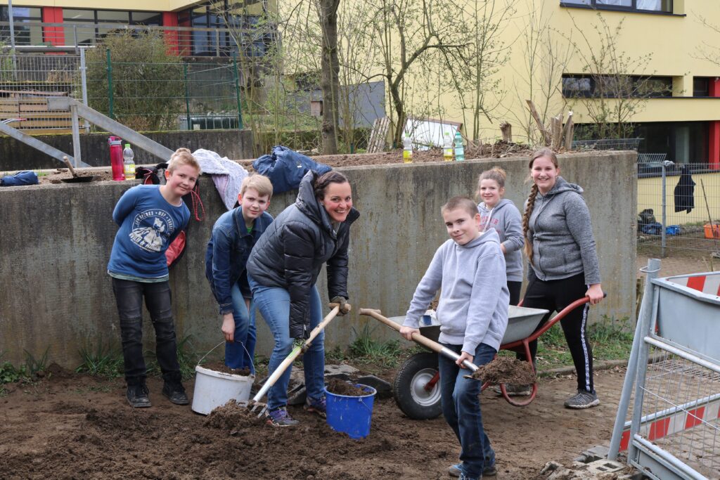 Sechs Personen arbeiten gemeinsam im Freien und graben Erde um.