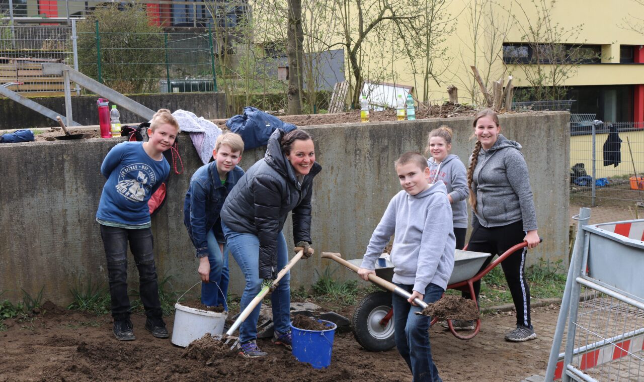 Sechs Personen arbeiten gemeinsam im Freien und graben Erde um.