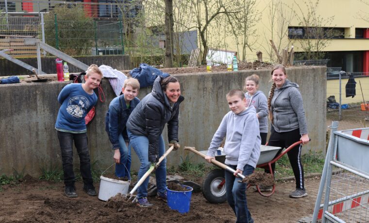 Sechs Personen arbeiten gemeinsam im Freien und graben Erde um.
