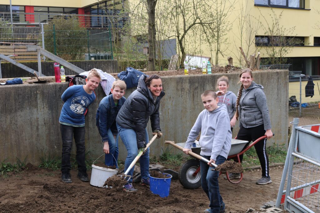 Schüler und Lehrkräfte arbeiten gemeinsam im Garten.