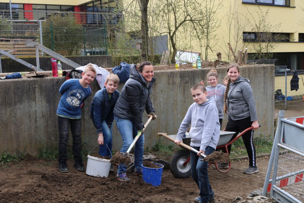 Sechs Personen arbeiten gemeinsam im Freien mit Schaufeln und Eimern.