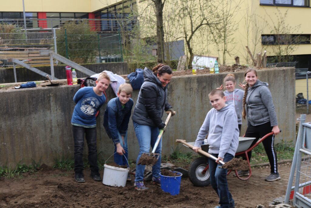 Schüler und Lehrer arbeiten gemeinsam im Freien und graben Erde aus.