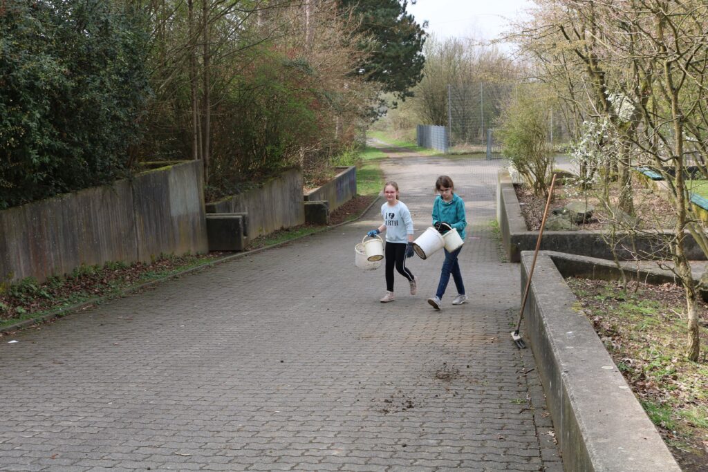 Zwei Kinder gehen einen Weg entlang und tragen Eimer.