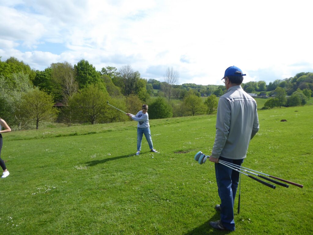 Person spielt Golf auf einer grünen Wiese, andere Person schaut zu.