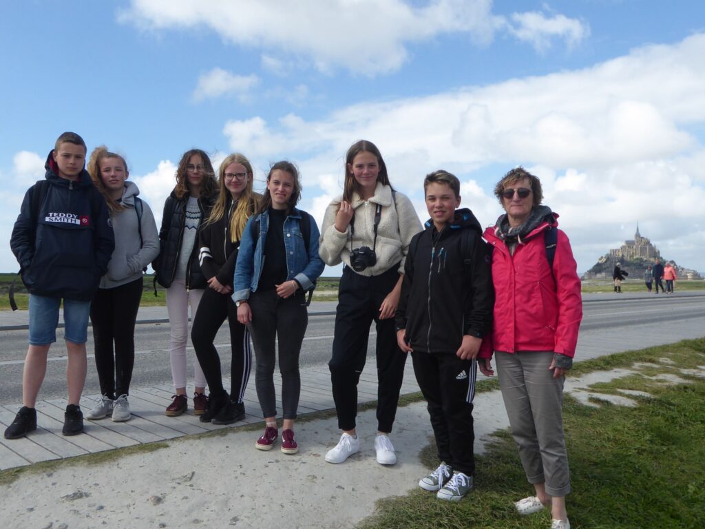 Gruppe von Schülern und Erwachsenen steht an der Straße mit Mont Saint-Michel im Hintergrund.
