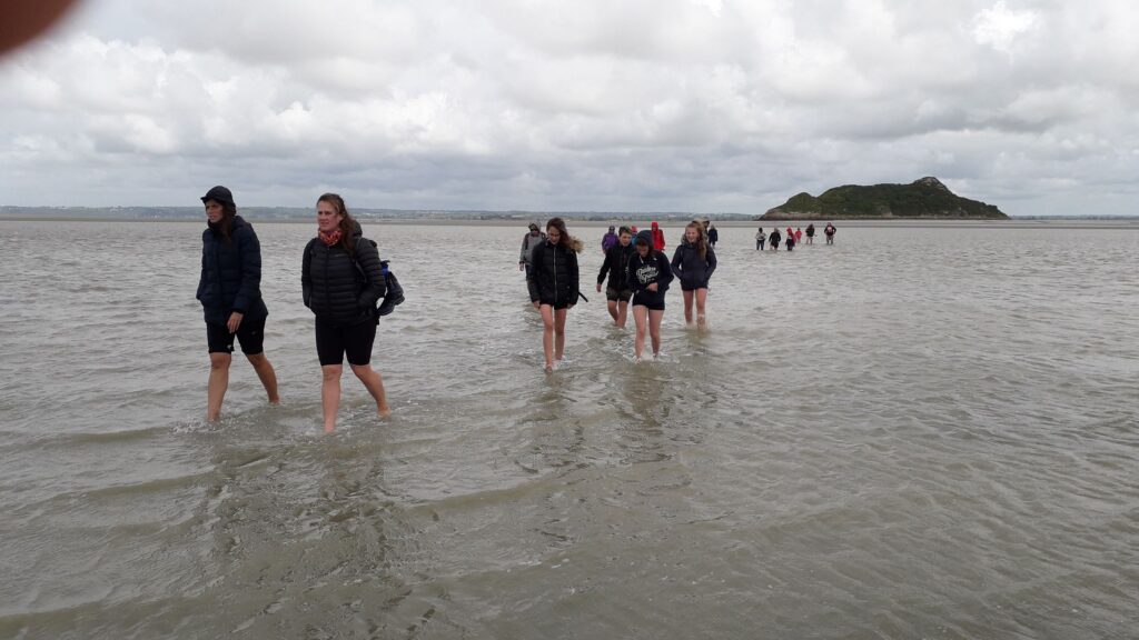 Gruppe von Menschen, die im flachen Wasser bei bewölktem Himmel spazieren.