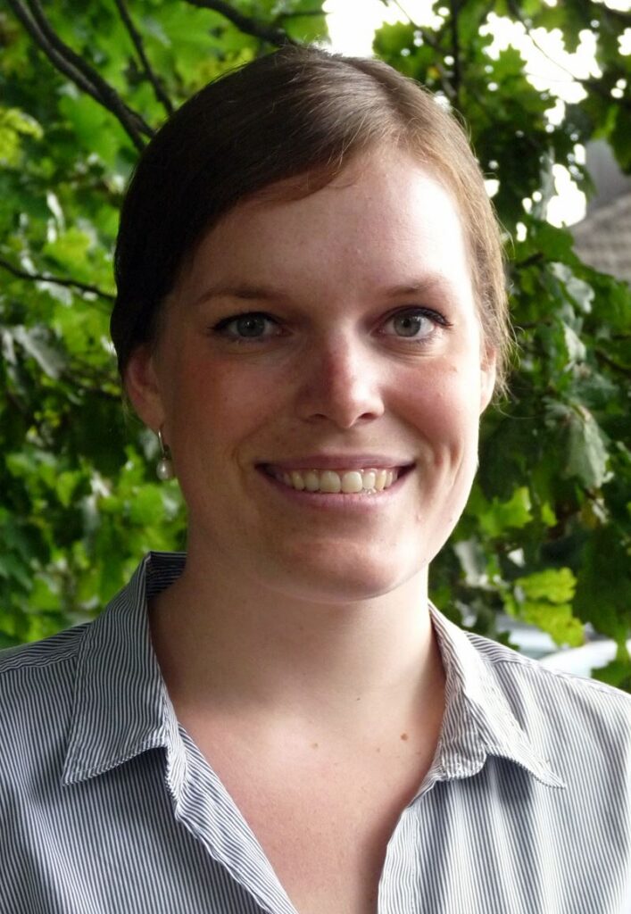 Portrait einer lächelnden Frau vor einer grünen Hintergrund mit Bäumen.