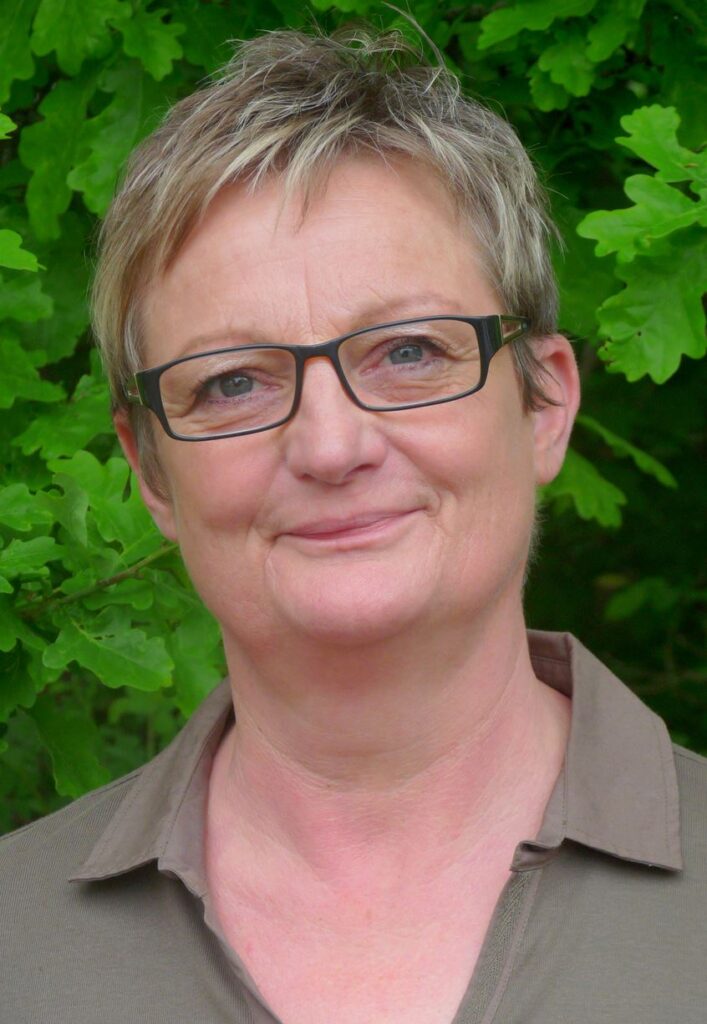 Frau mit Brille und kurzem Haar vor grünem Hintergrund.