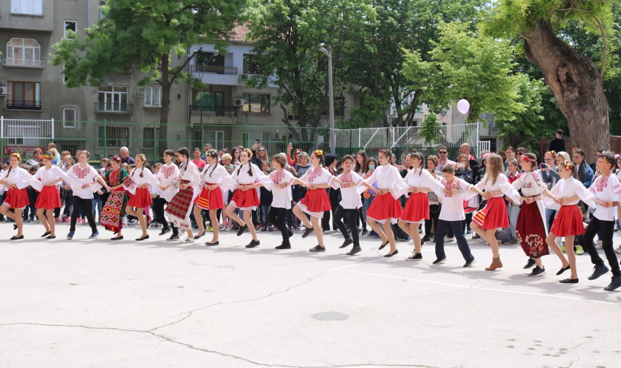 Tanzende Gruppen in traditionellen Kostümen auf einem Schulhof.