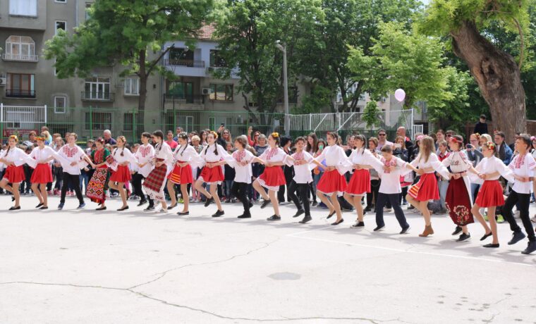 Tanzende Gruppen in traditionellen Kostümen auf einem Schulhof.