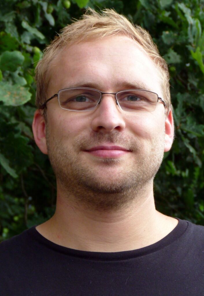 Ein Mann mit Brille steht vor einem grünen Hintergrund.