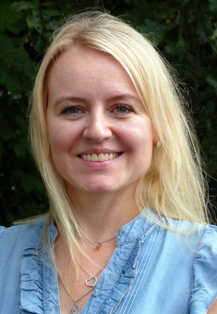 Frau mit blonden Haaren und lachendem Gesicht vor grüner Hintergrund.