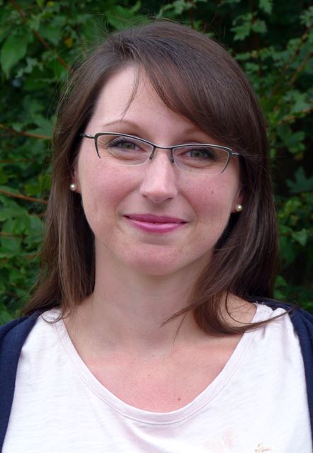 Frau mit Brille und langen Haaren vor grünem Hintergrund.