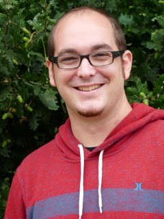 Mann mit Brille und rotem Sweatshirt vor grünem Hintergrund.