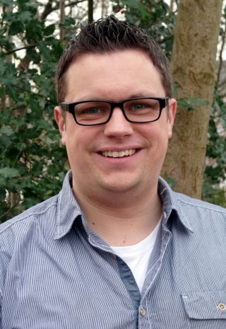 Lächelnder Mann mit Brille vor einem grünen Hintergrund.