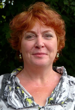 Eine lächelnde Frau mit roten Haaren vor einem grünen Hintergrund.