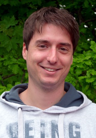 Lächelnder Mann mit braunen Haaren vor grünem Hintergrund.