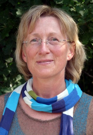 Eine Frau mit blonden Haaren und Brille trägt einen bunten Schal.
