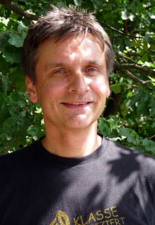 Ein Mann mit kurzem, dunklem Haar steht vor einem grünen Hintergrund.