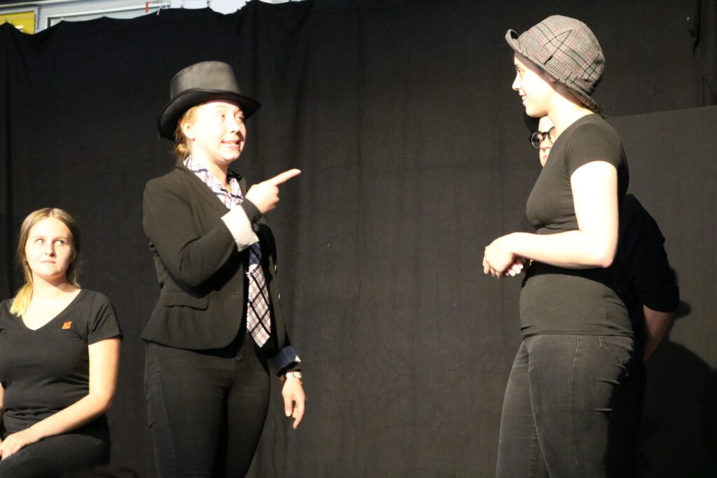 Zwei Schauspielerinnen führen einen Dialog auf einer Theaterbühne auf.