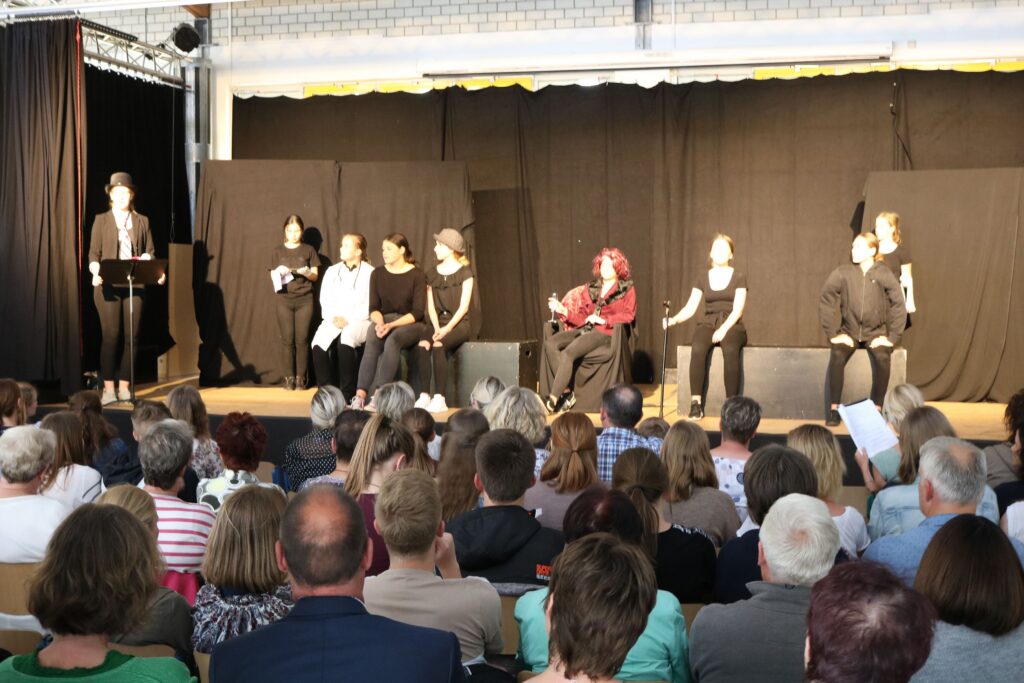 Schüler führen ein Theaterstück auf einer Bühne vor Publikum auf.