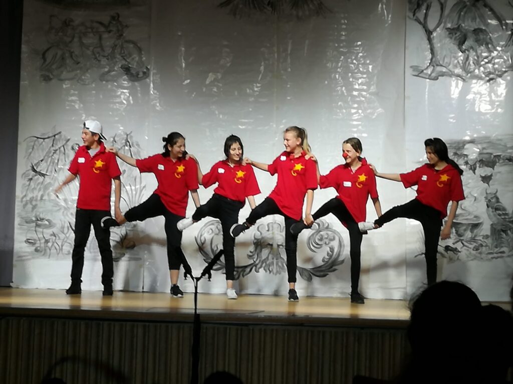 Sechs Tänzerinnen in roten T-Shirts führen eine Choreografie auf.