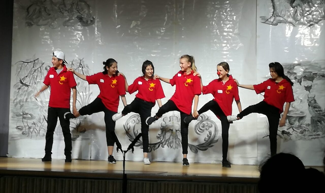Sechs Tänzerinnen in roten T-Shirts führen eine Choreografie auf.