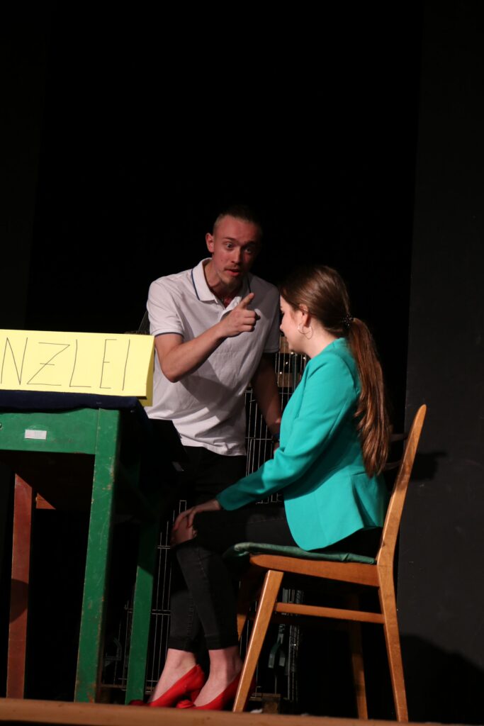 Szenische Aufführung mit zwei Schauspielern an einem Tisch.