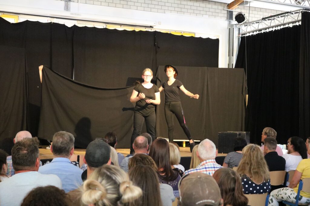 Zwei Personen führen einen Tanz oder eine Theateraufführung auf einer Bühne vor Publikum auf.
