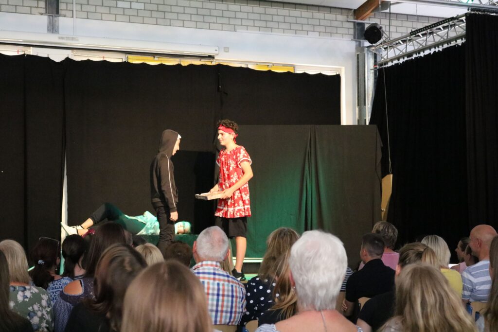 Schülervorführung auf der Bühne mit Schauspielern und Publikum.