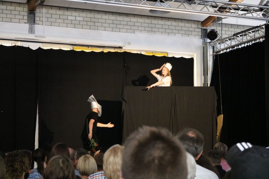 Theateraufführung mit zwei Personen auf der Bühne, Zuschauer im Vordergrund.