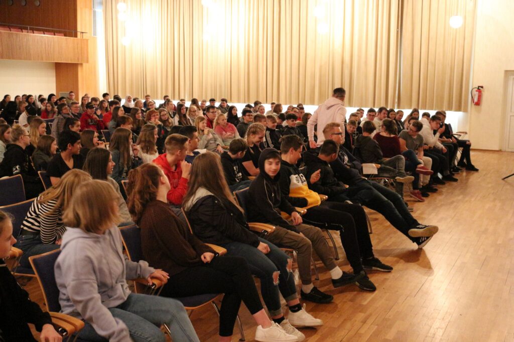 Schüler sitzen in einem großen Saal und lauschen einer Veranstaltung.