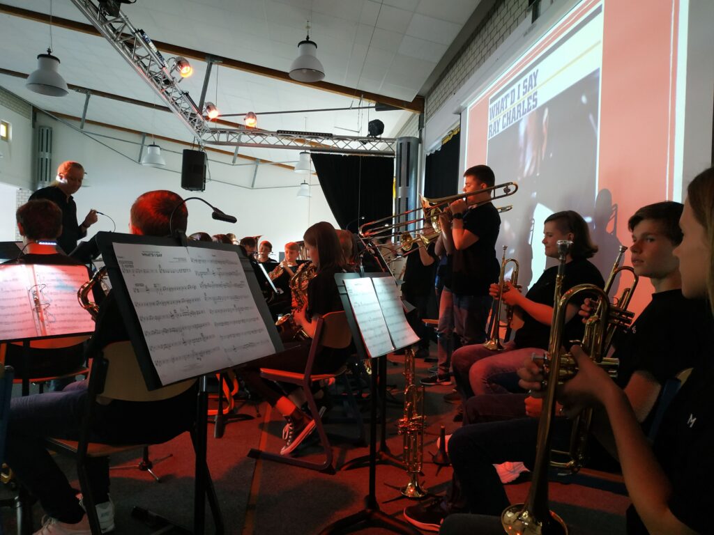 Schulorchester spielt auf der Bühne, Notenständer und Instrumente sichtbar.
