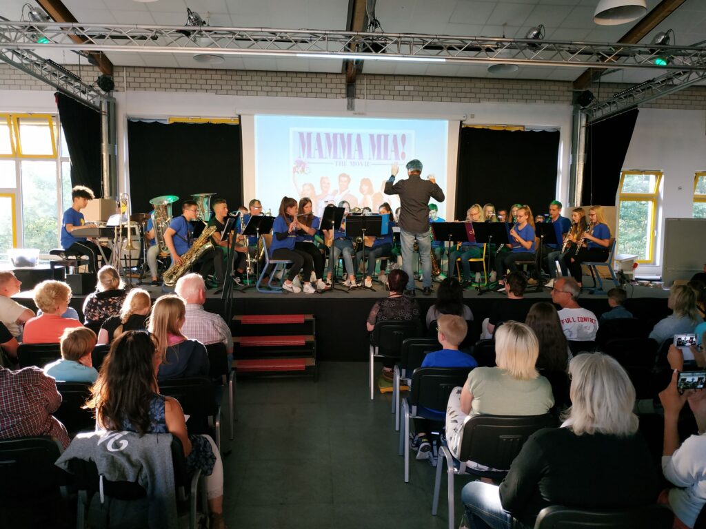 Schülerband spielt auf Bühne vor Publikum in einem Saal.