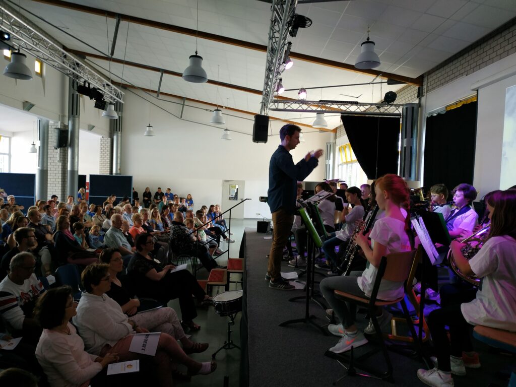 Ein Orchester spielt vor einem großen Publikum in einem Veranstaltungssaal.